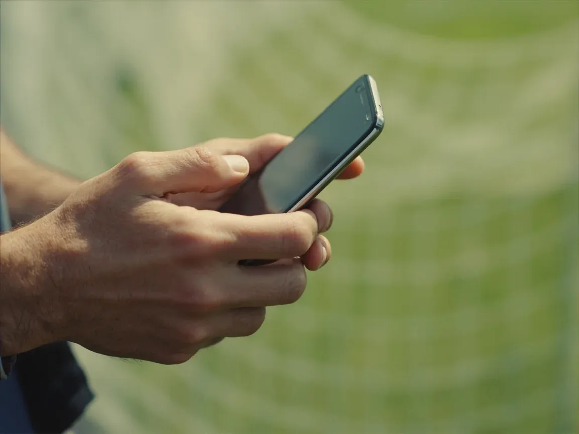 Editorial photograph of an adult navigating the app on a generic phone, with screen turned away and a notebook beside it.